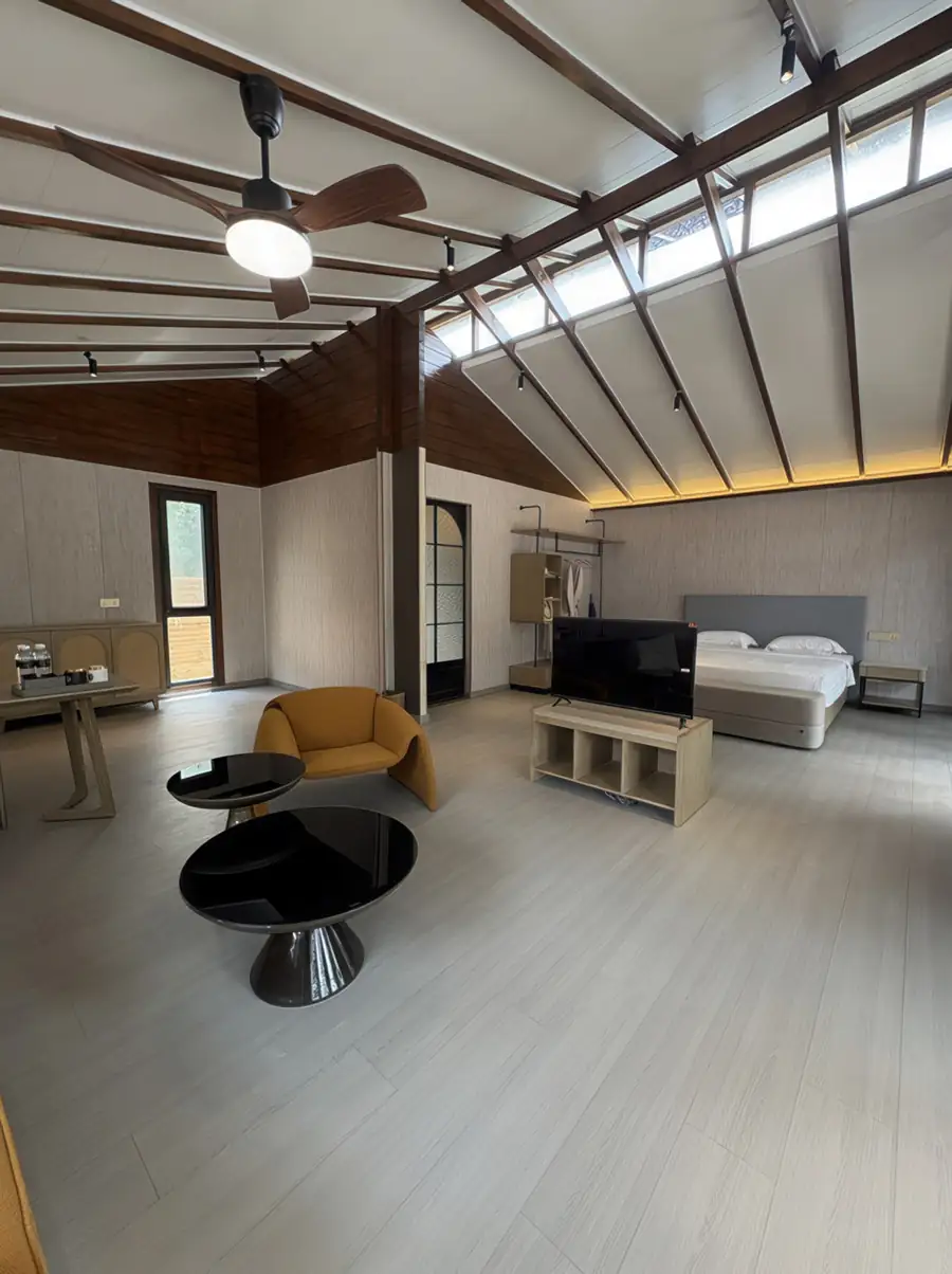 A vast bedroom at Doris Mataking Resort where a king bed faces a TV stand with light timber flooring and vaulted ceilings
