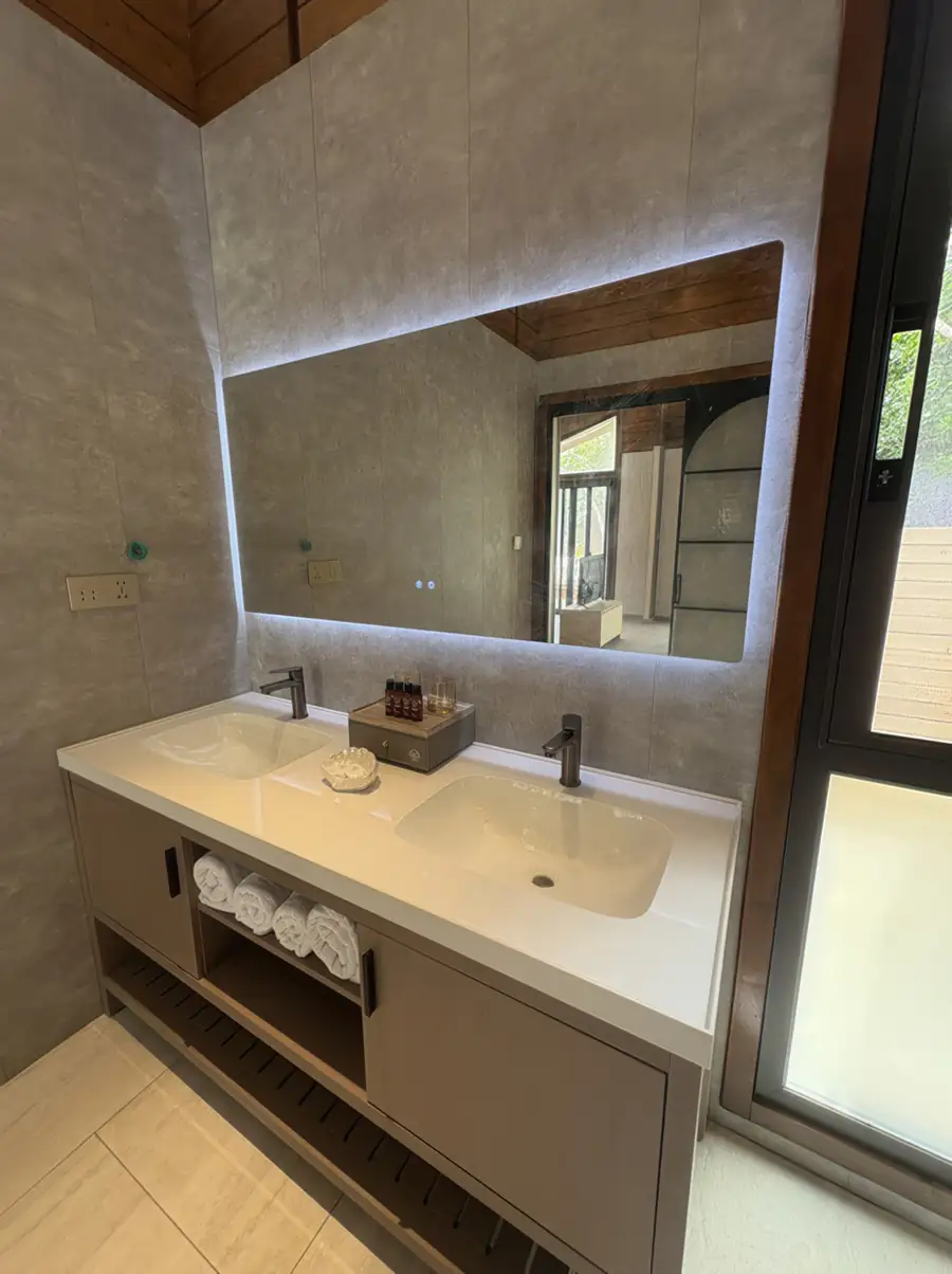 A spacious bathroom at Doris Mataking Resort with a wooden double vanity, round mirrors and marble-patterned wall tiles