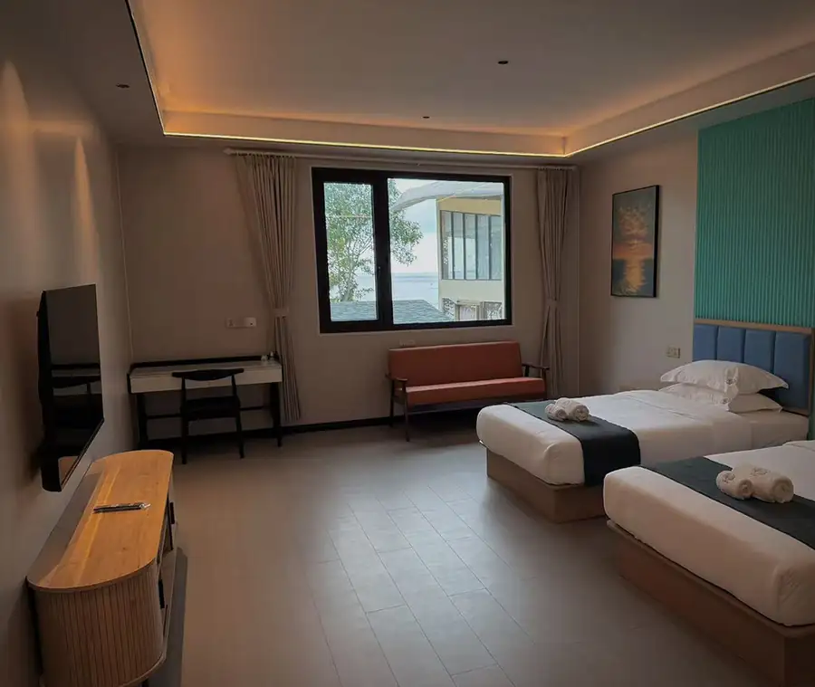 A bright twin bedroom at Doris Mataking Resort with two beds facing a large window with ocean views and wooden floors