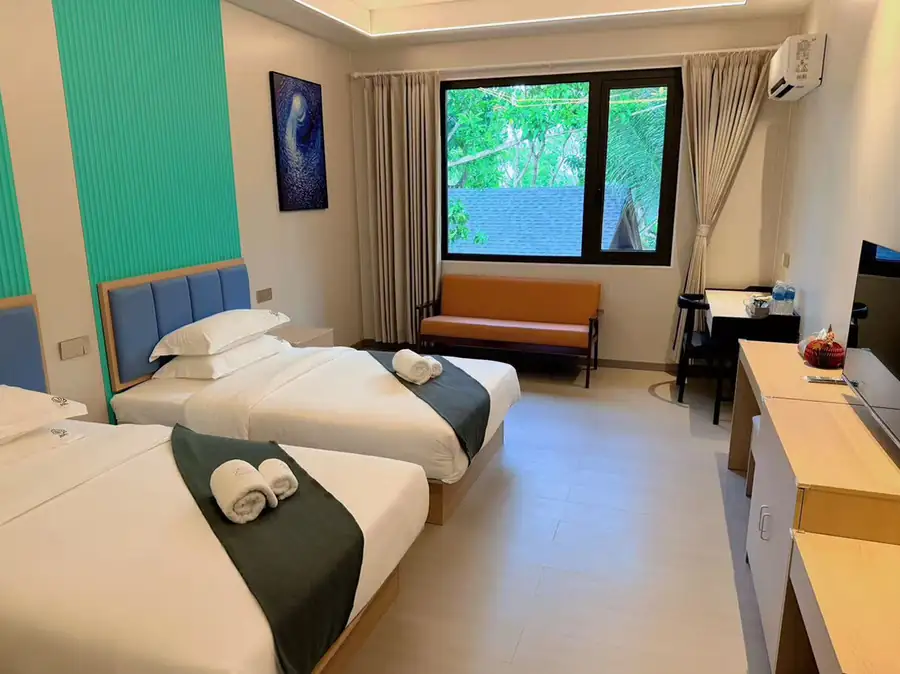 A bright twin bedroom at Doris Mataking Resort with beds facing a garden-view window and gleaming timber floors
