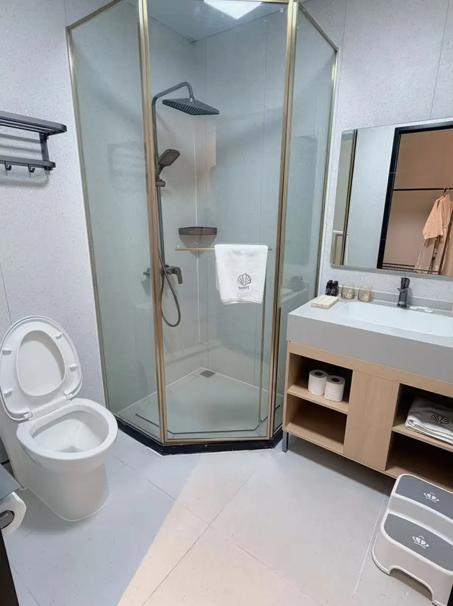 A stylish bathroom at Doris Mataking Resort with marble wall tiles, dark vanity, round mirror and glass-partitioned shower