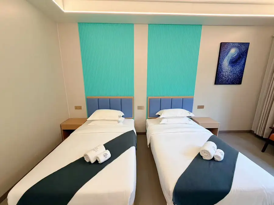 A modern twin bedroom at Doris Mataking Resort with a symmetrical layout, turquoise headboard panels and wooden flooring
