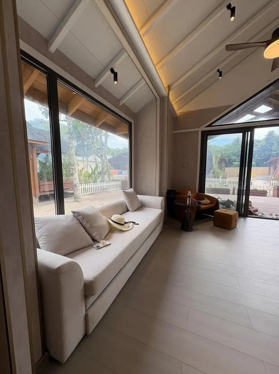 A bright lounge area at Doris Mataking Resort with an expansive sofa by panoramic glass doors opening onto the garden