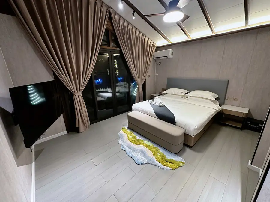 A serene bedroom at Doris Mataking Resort featuring a large bed facing seamless glass doors at twilight with warm wooden flooring